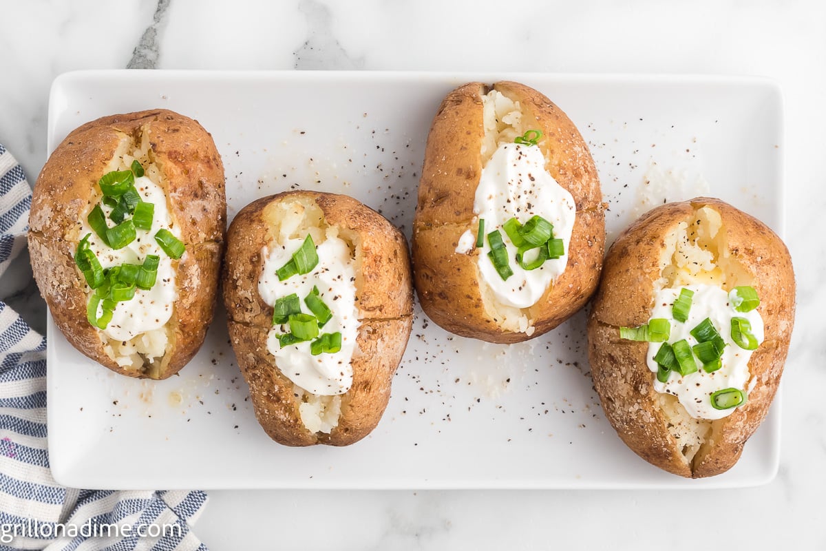 Smoked baked potatoes on a white platter topped with sour cream and chives