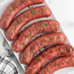Six sausages on a white plate with parsley.