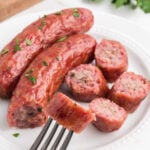 Sausage on a fork with parsley on a white plate.