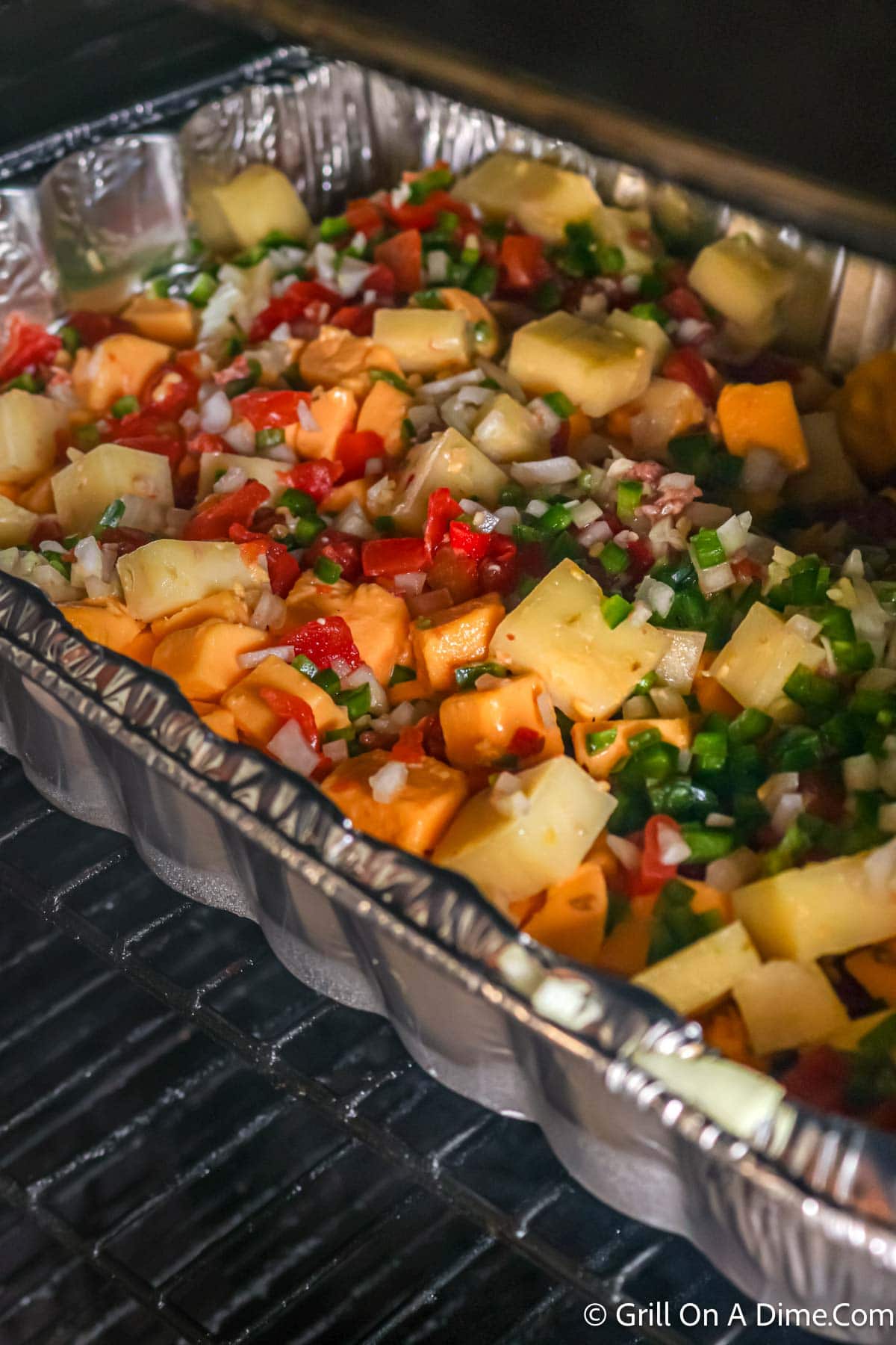 Queso ingredients in a aluminum pan placed on the grill grates on the grill