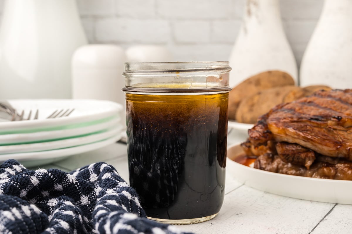 3 ingredient steak marinade in a glass jar with plate stacked with grilled steaks.