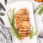 Grilled pork chops on a white plate with rosemary sprigs.