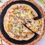 A pizza with cheese, meat and vegetables on a black plate.