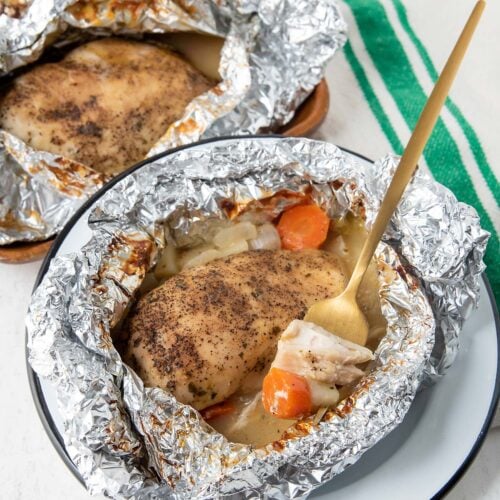 Cooked Chicken Breast in Foil with cooked onions and carrots on a plate
