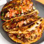 Smash Tacos stacked on a plate topped with pico de gallo