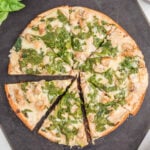 A sliced Blackstone chicken alfredo pizza on a dark cutting board, with melted cheese and large pieces of spinach visible on top.