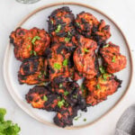 Cooked chicken thighs with a red color that is stacked on a plate.