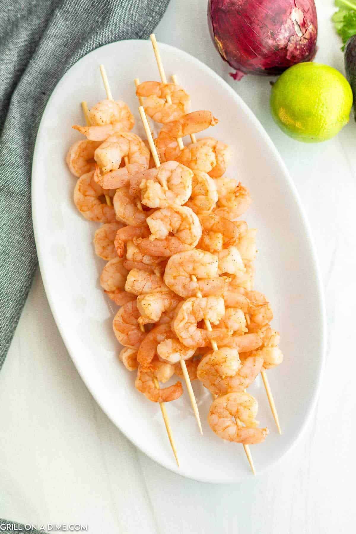 Marinated shrimp on skewers stacked on a white platter. 