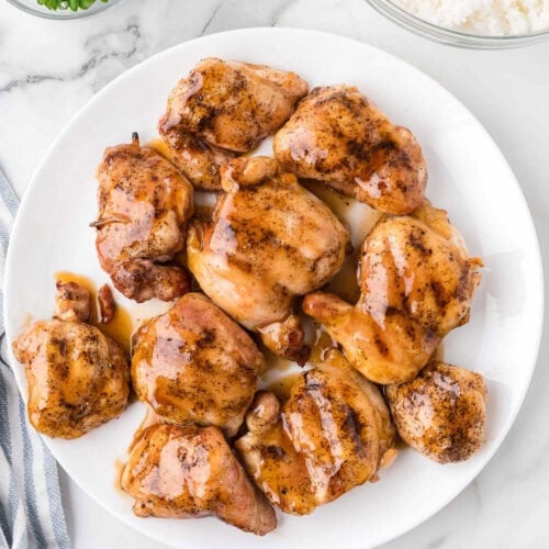 Juicy, seasoned chicken thighs glazed with honey on a white plate for a flavorful meal.