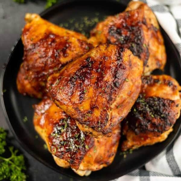 BBQ chicken thighs stacked on a plate.