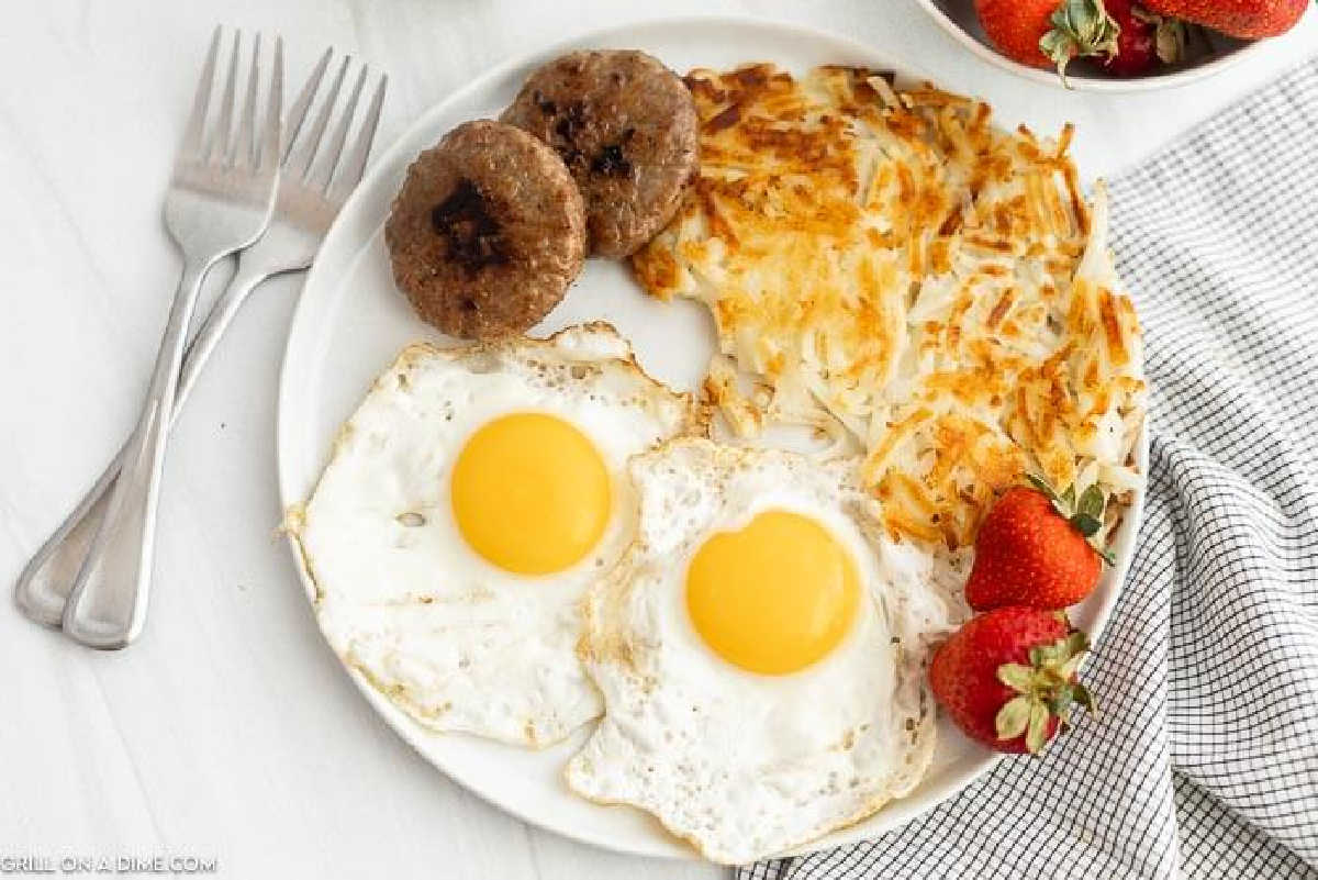 A breakfast plate with two Fried Eggs, two sausage patties, hash browns, and two strawberries. 