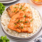 Baked salmon fillets garnished with fresh herbs served over white rice on a white plate.