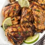 Grilled chicken thighs stacked on a white plate topped with chopped herbs.