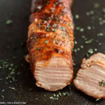 Bacon wrapped pork tenderloin on a black platter.