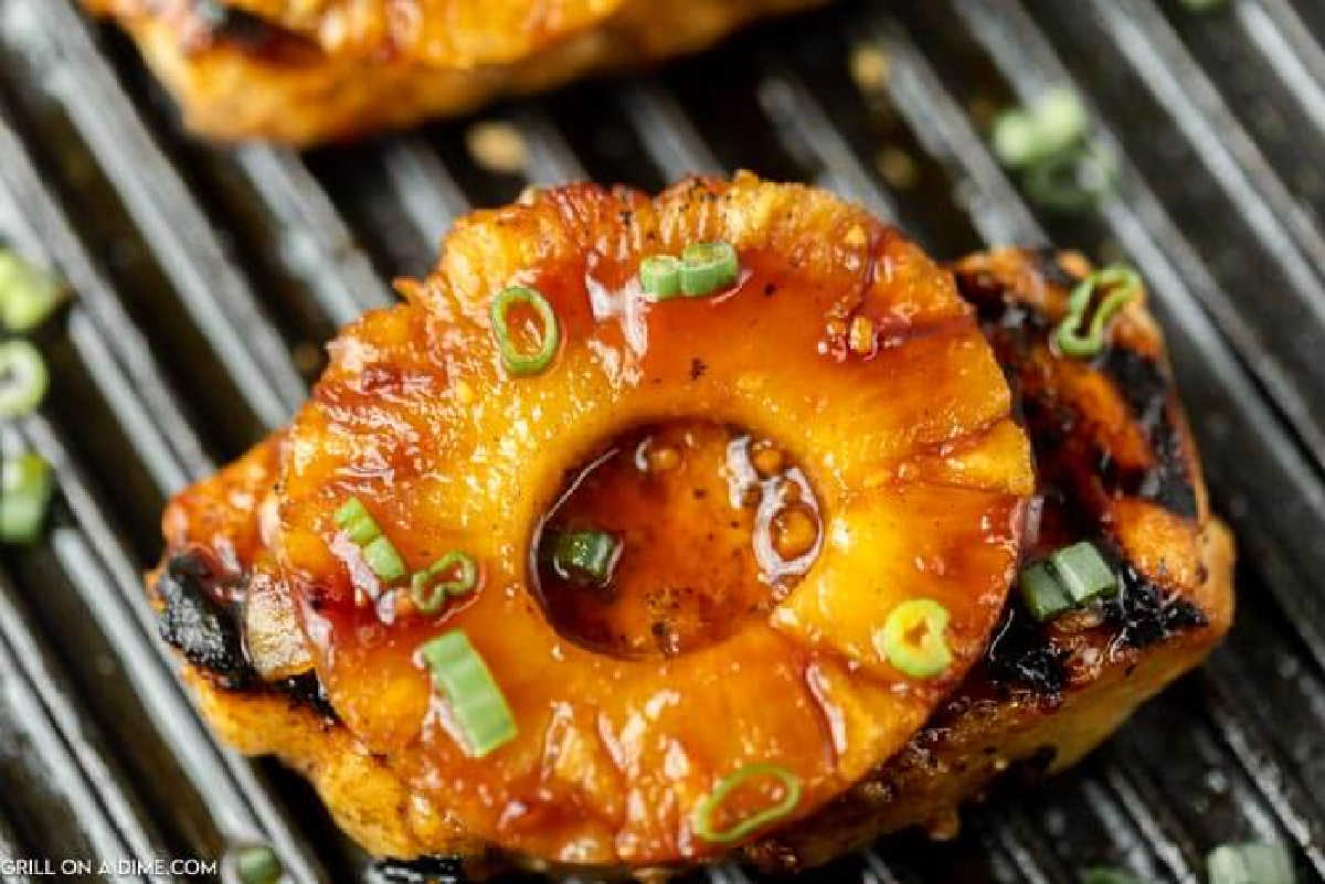 Grilled Hawaiian Pork Chops, with grilled pineapple ring topped with chopped green onions, resting on the grill with visible grill marks.