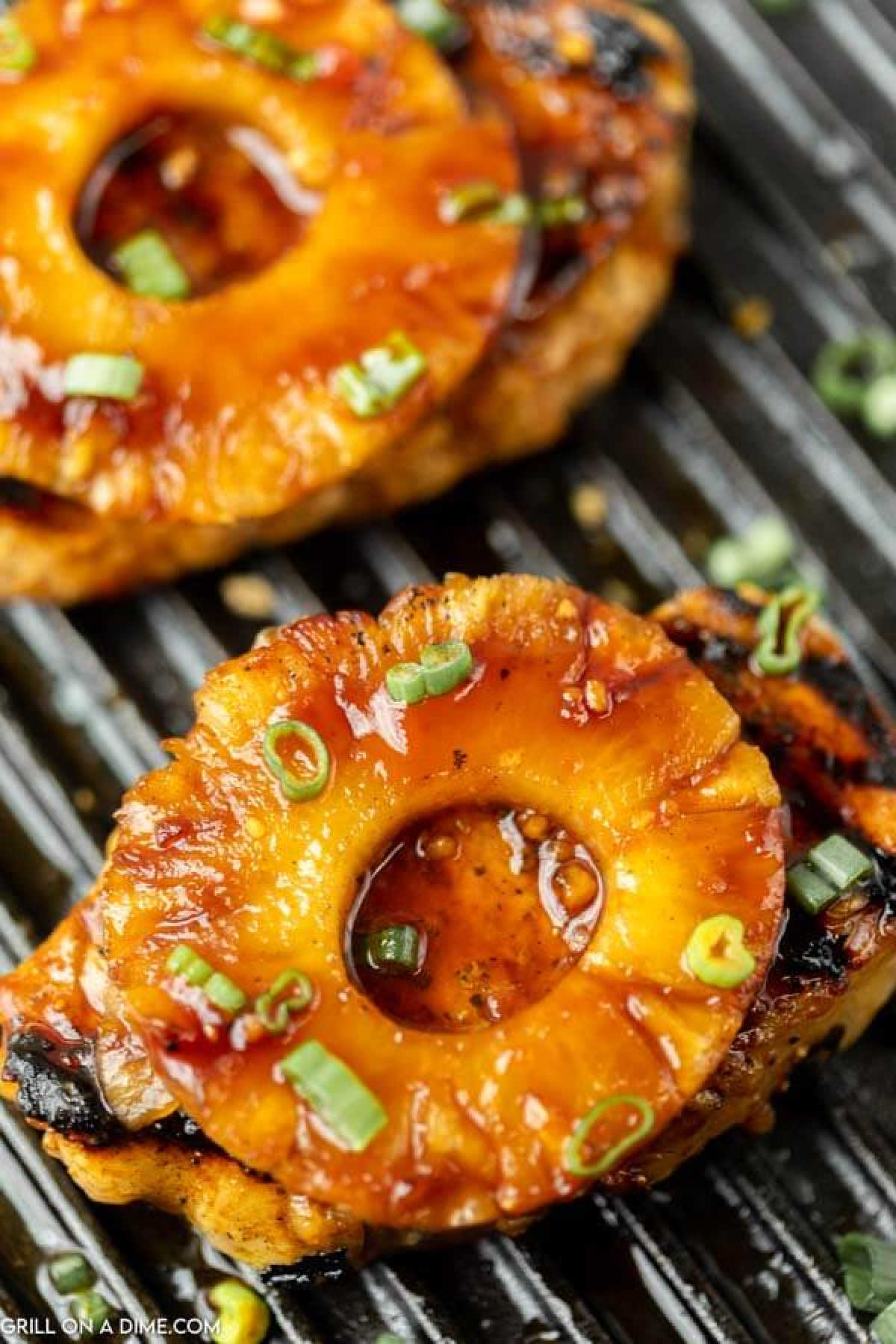 Grilled pork chops topped with caramelized pineapple rings and sprinkled with chopped green onions, served on a grill pan.