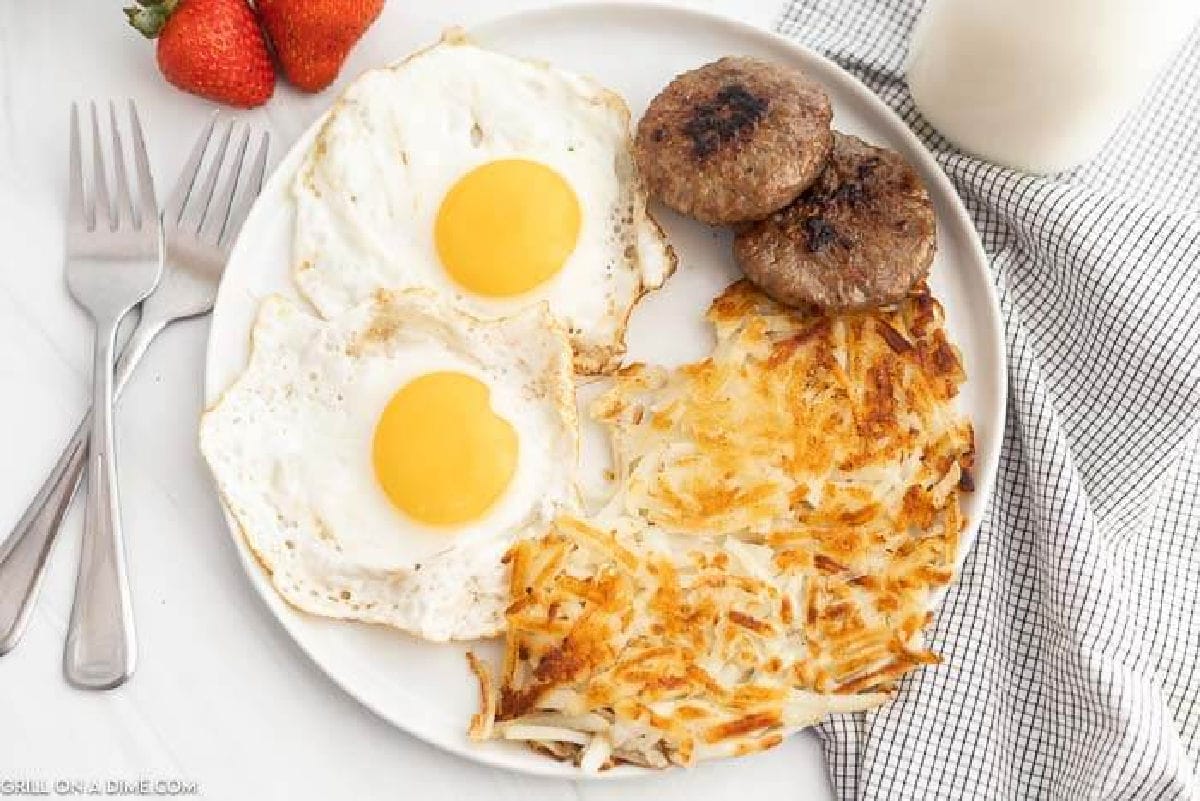 Crispy hashbrowns on a plate with a side of eggs and sausage patties. 