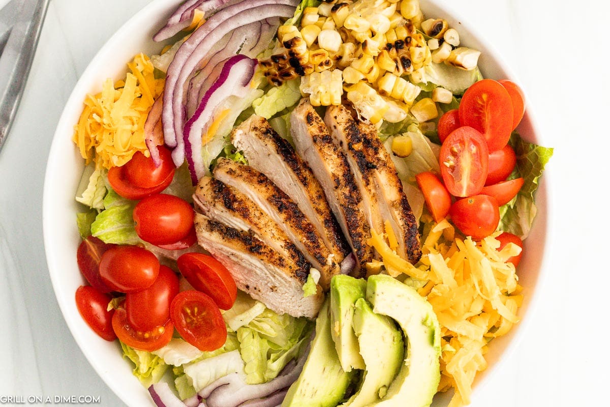 Grilled Chicken Salad topped with red onions, roasted corn, cherry tomatoes, and avocados. 