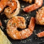 Grilled Shrimp topped with salt on a black surface.