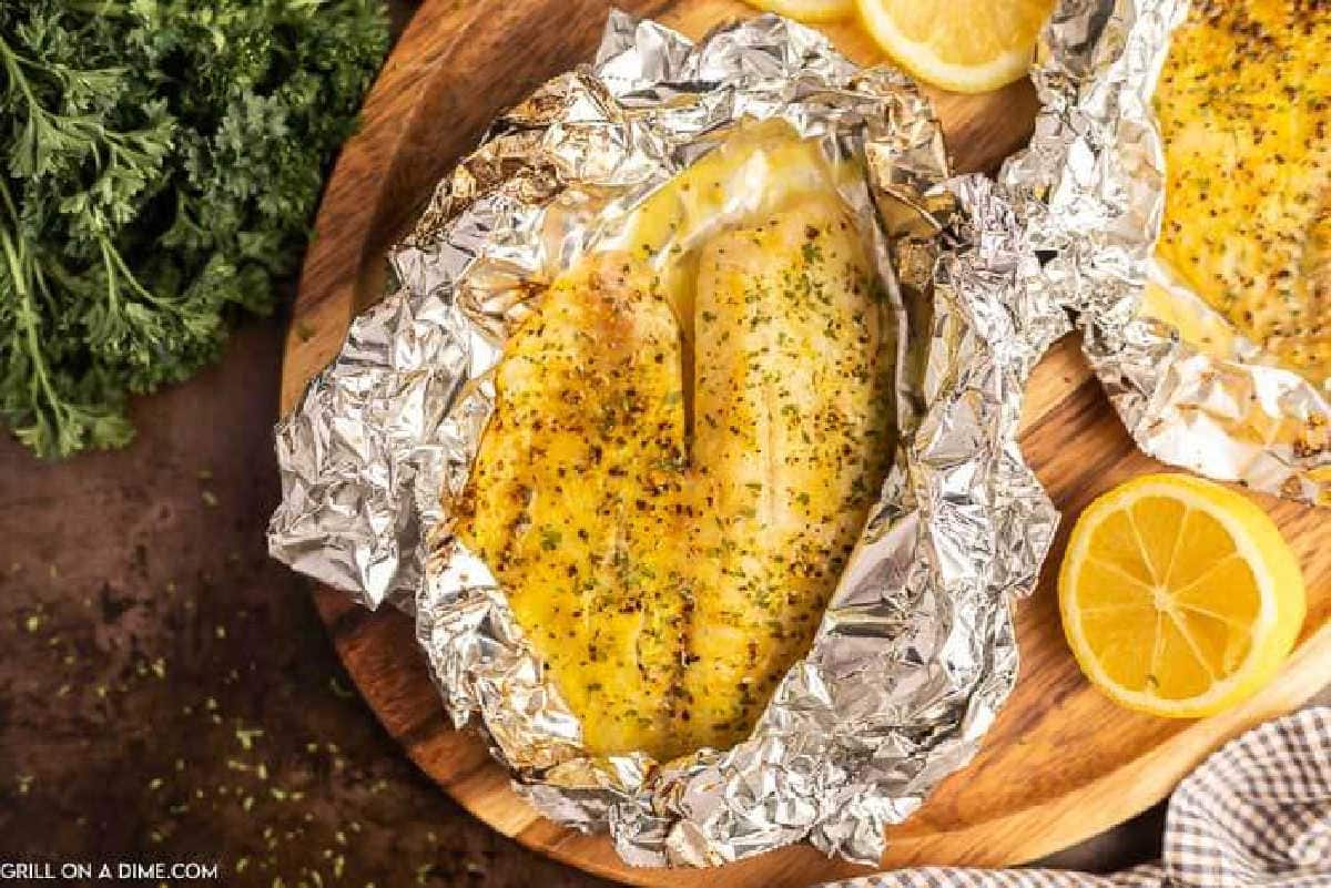Tilapia in foil on a wooden platter with a side of lemon wedges