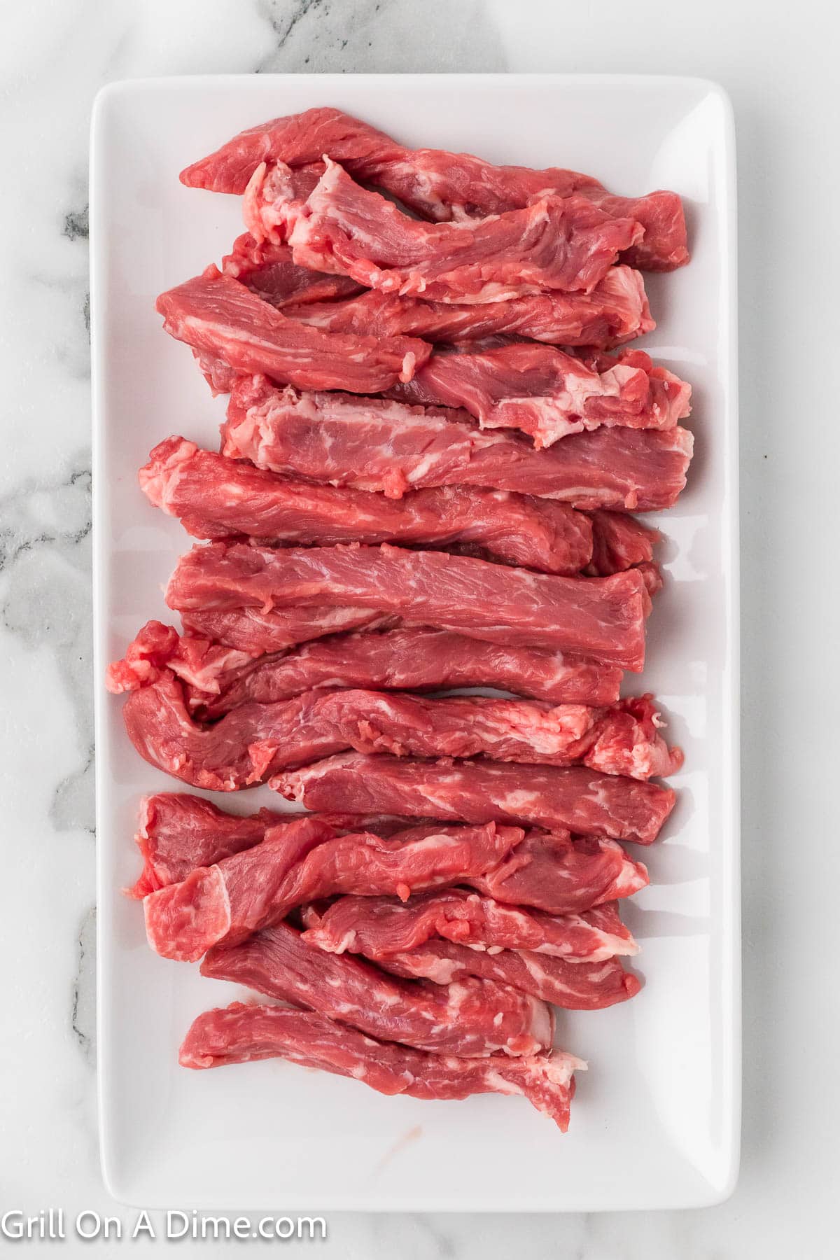 Uncooked steak cut into strips on a white platter