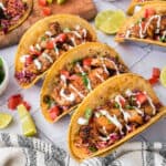Grilled fish tacos with toppings on corn tortillas, fresh lime wedges, and colorful sides.