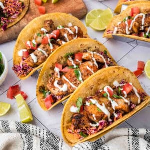 Grilled fish tacos with toppings on corn tortillas, fresh lime wedges, and colorful sides.