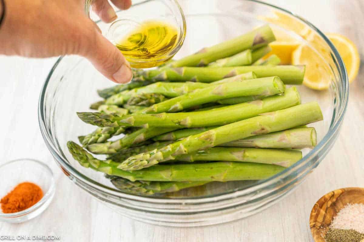 Asparagus in a clear bowl with oil being poured over.