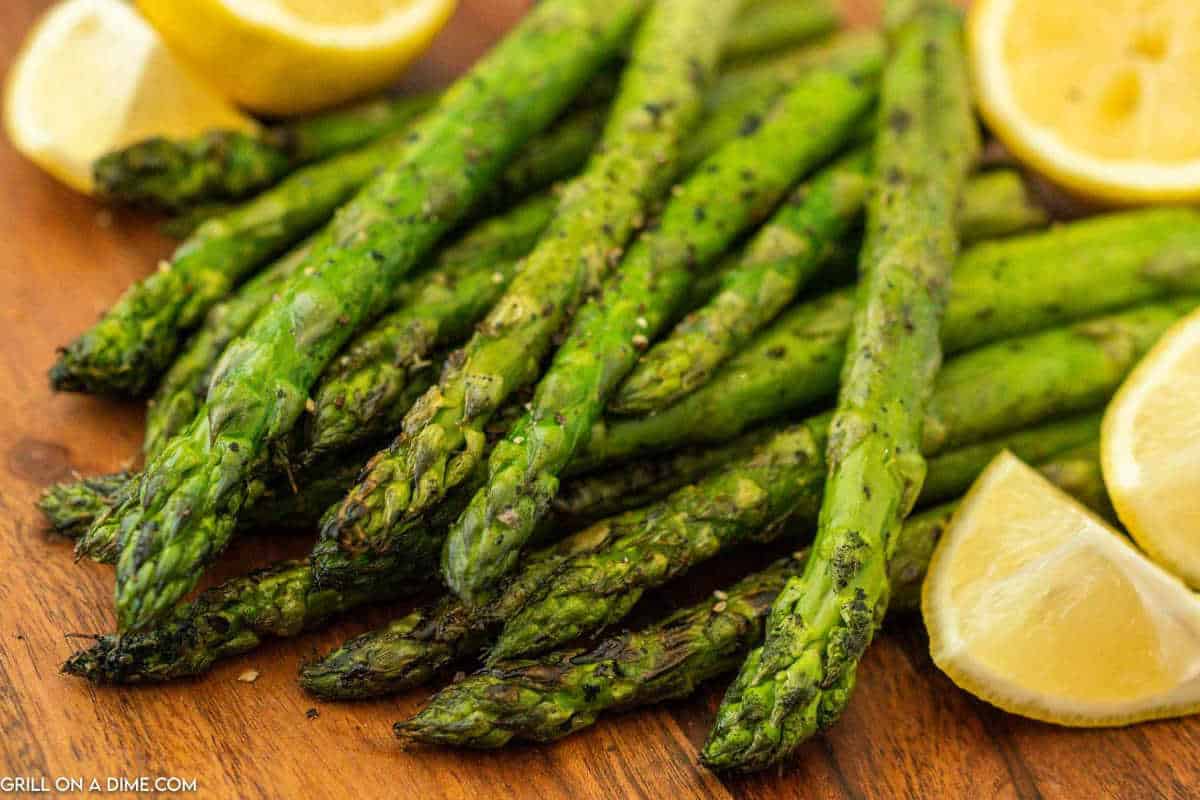 Asparagus stacked on a wooden platter with fresh lemon wedges on the side.