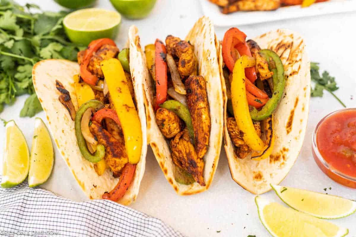 3 Chicken Fajitas Tacos with lime wedges and a bowl of salsa on the side.