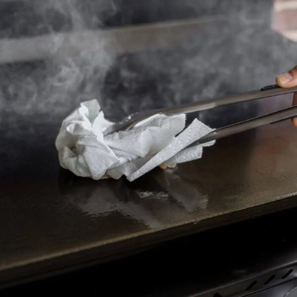 A person using a spatula to clean a grill.
