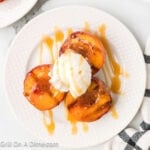 Grilled Peaches on a white plate topped with ice cream and a drizzle of caramel sauce