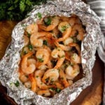 Shrimp in foil packets on a wooden cutting board.