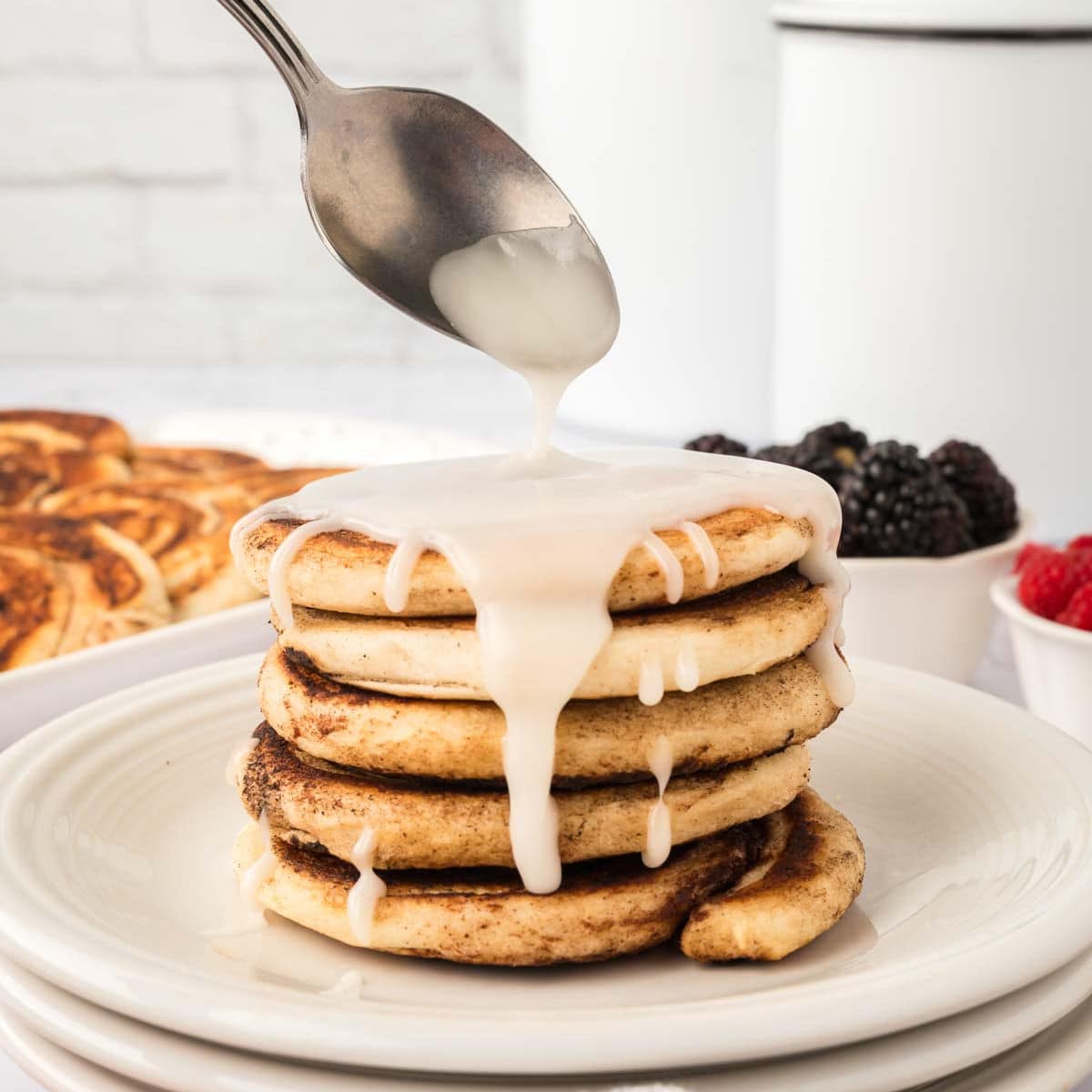 Cinnamon Roll Pancakes stacked on a plate and topped with icing