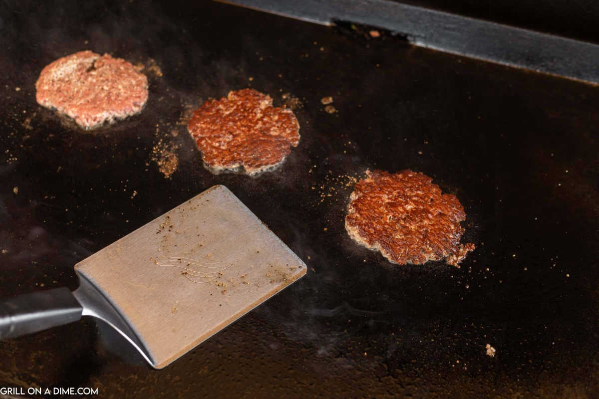 Hamburger patties on the griddle with a spatula.