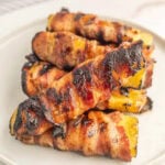 Grilled bacon-wrapped chicken thighs with charred grill marks on a white plate