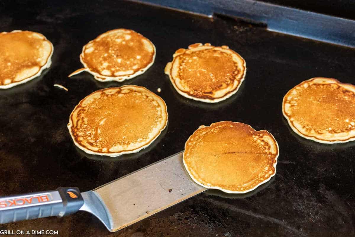 Cooking pancakes on a Blackstone and flipping with a spatula.