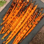 Grilled carrots on a slate board with herbs.