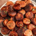 A plate of cooked sausages with herbs on top.