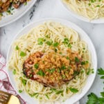 Juicy chicken thigh with breadcrumb topping served over spaghetti pasta in a white bowl.