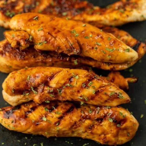 Juicy grilled chicken breasts with herbs on black plate.