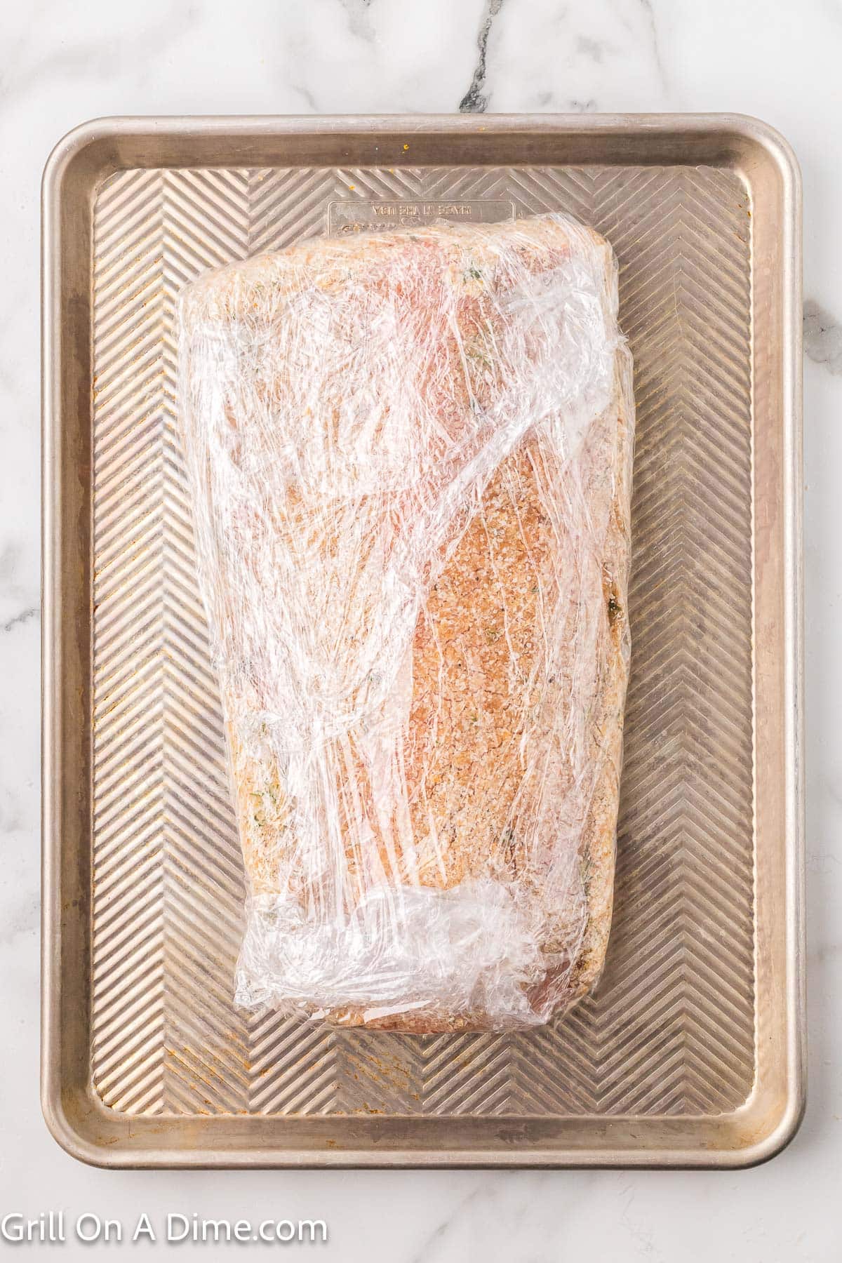 Seasoned Salmon wrapped in plastic wrap on a baking sheet