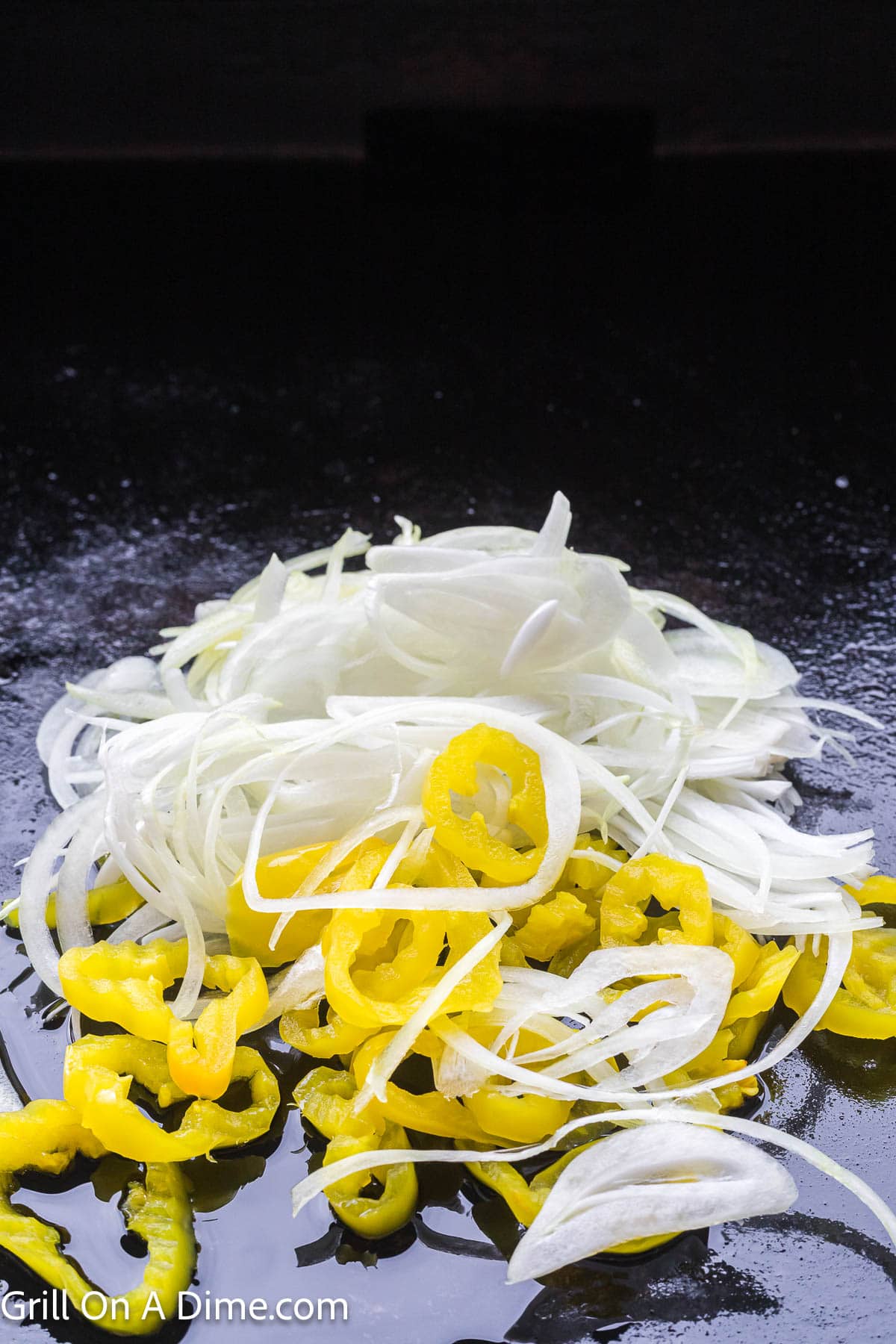 Sliced onions and yellow pepper cooking on the griddle with oil