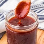 Sweet homemade BBQ sauce in a glass jar with a wooden spoon. Perfect for grilled meats and sandwiches.