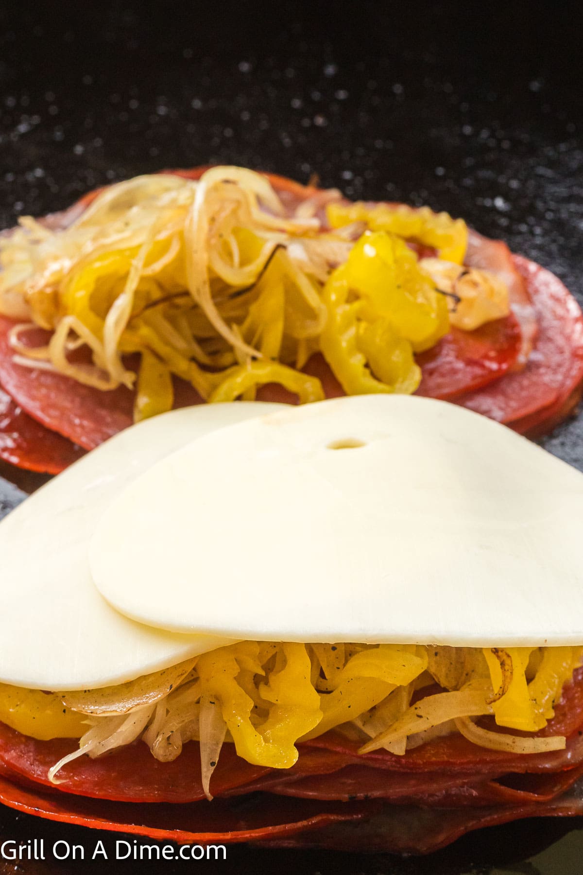 Deli meat topped with yellow peppers and grilled onions topped with slice provolone cheese