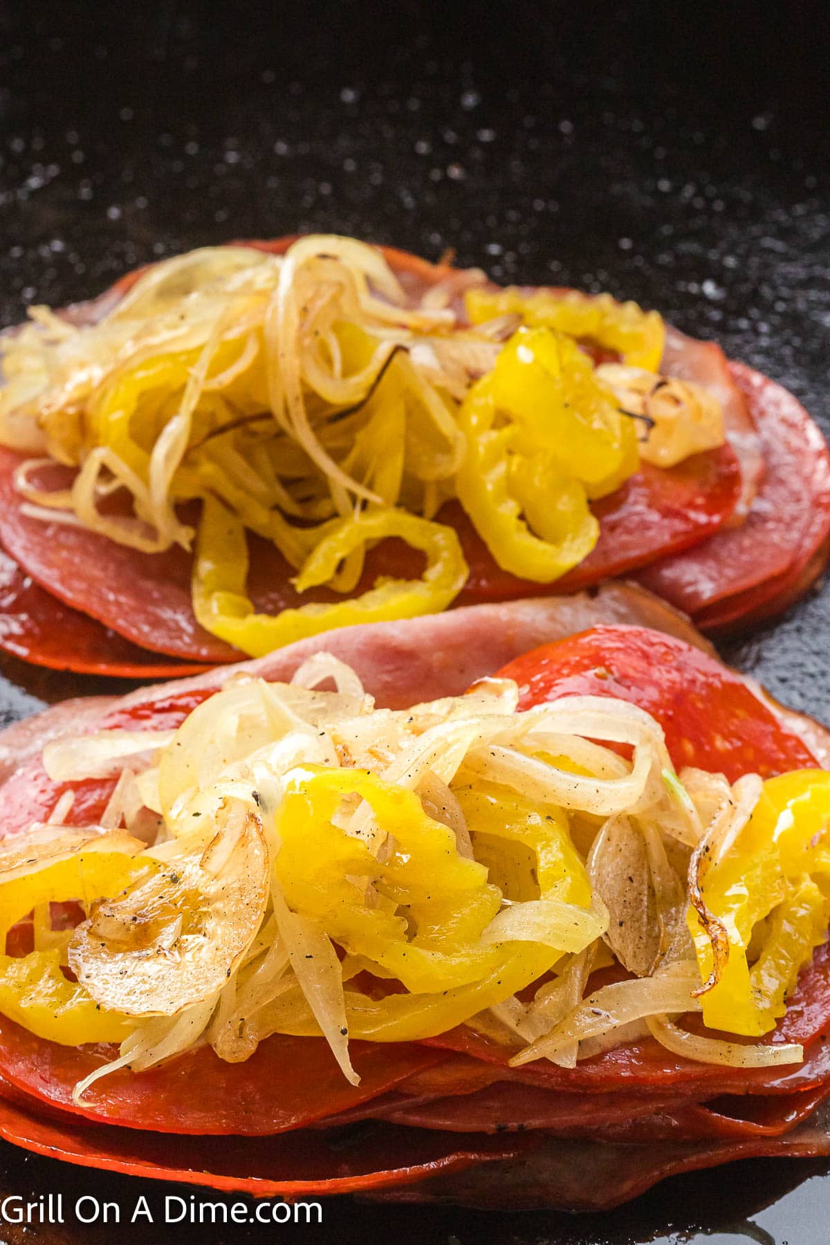 Slice deli meat in a pile topped with grilled onions and yellow peppers on the griddle