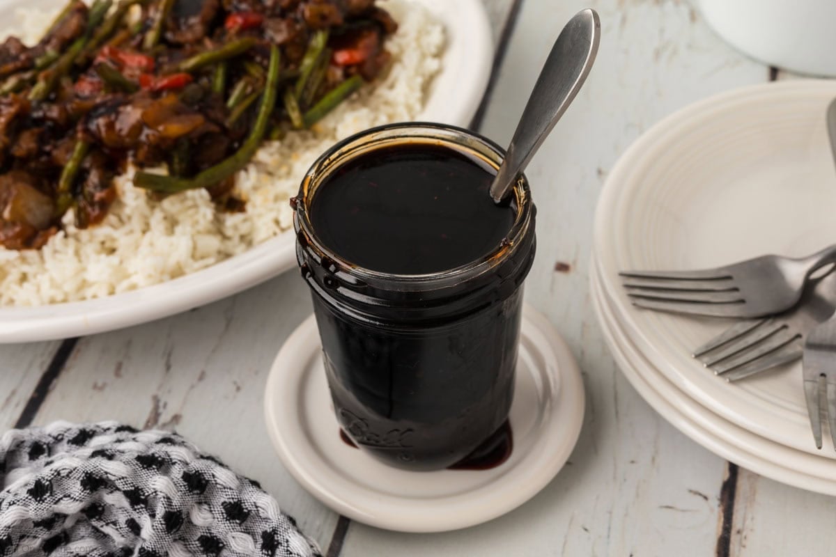 Korean BBQ Sauce in a clear jar with a plate of stir fry over rice nearby.
