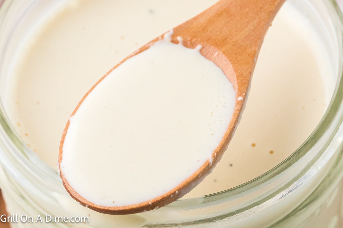 White sauce in a jar with a serving on a wooden spoon