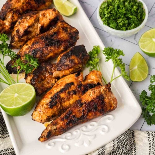 Grilled chicken drumsticks with fresh lime and herbs on a white platter