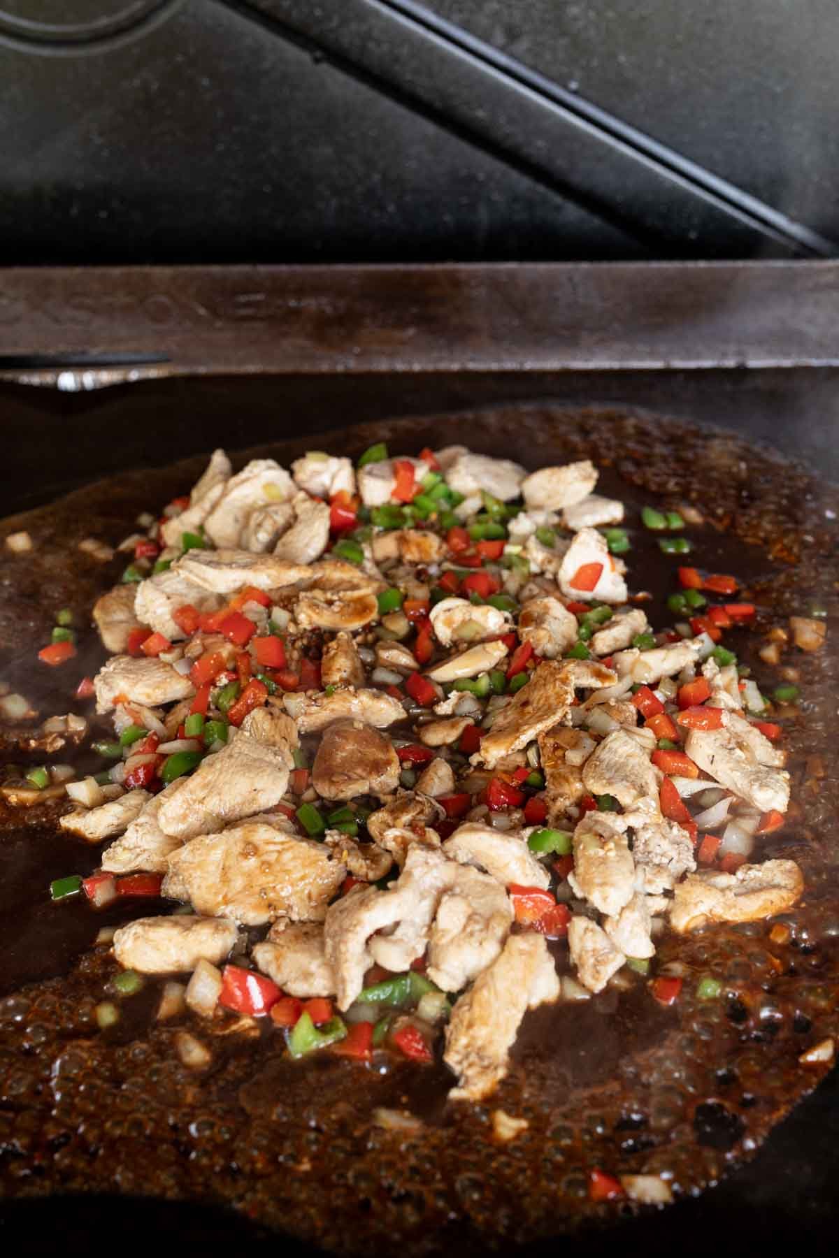 Pouring the sauce over the chicken and veggie mixture on the Blackstone Griddle